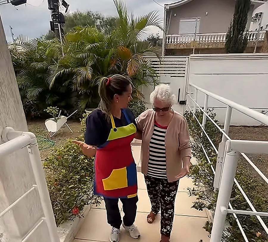 Cuidadora caminha de braço dado com uma aluna na rampa da entrada