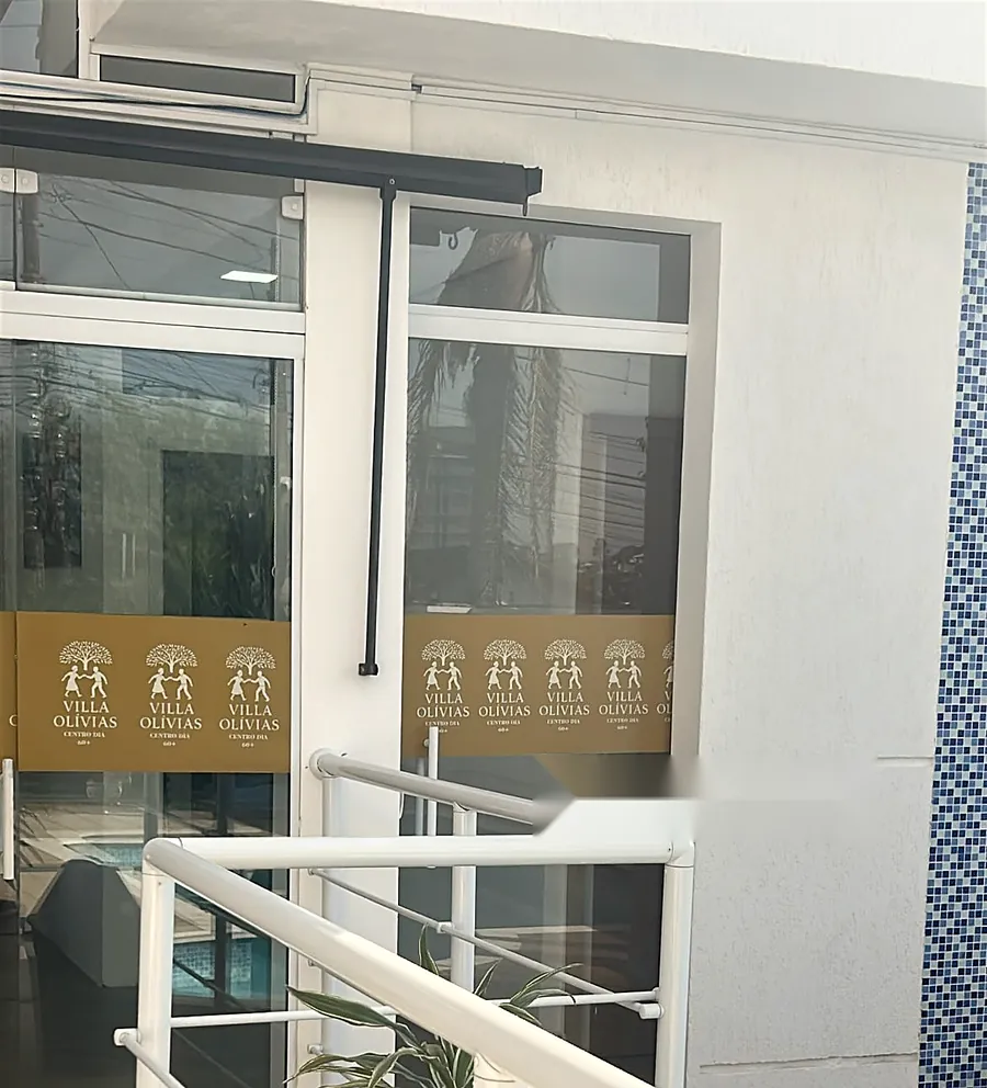 Entrada com portas de vidro, faixa da marca Villa Olívias e corrimão