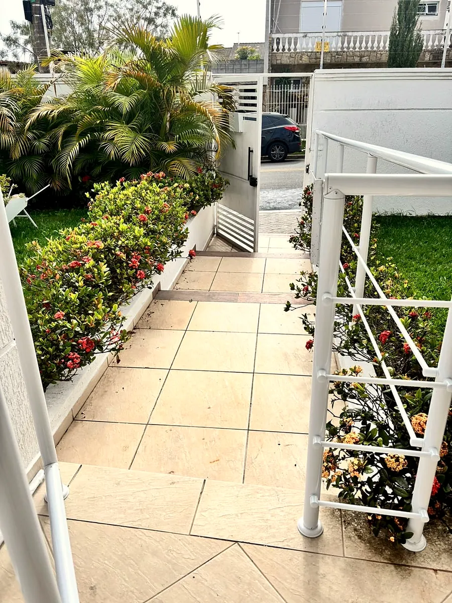 Rampa de entrada com corrimão branco e canteiros floridos