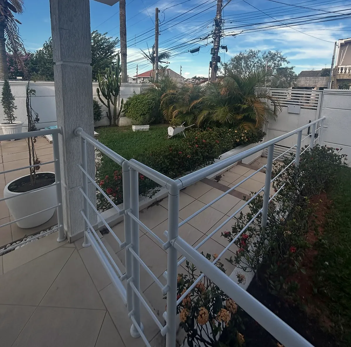 Varanda com guarda-corpo branco, jardim florido e céu azul